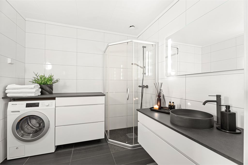 Badet i hovedetasjen har et stilrent uttrykk med lyse veggfliser og mørke detaljer.